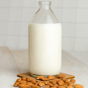 a glass bottle of nut milk resting on top of a pile of almonds