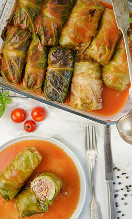 a baking dish of cabbage rolls next to a plate with halved cabbage roll on it.